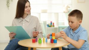 Young boy participating in a behavioral assessment with a healthcare professional while playing with colorful wooden blocks.